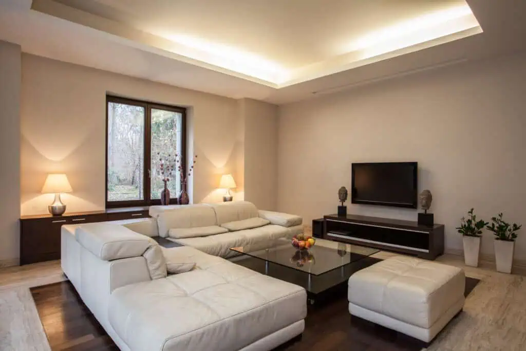 Modern living room with white sectional sofa, flat-screen TV, and minimalist decor.