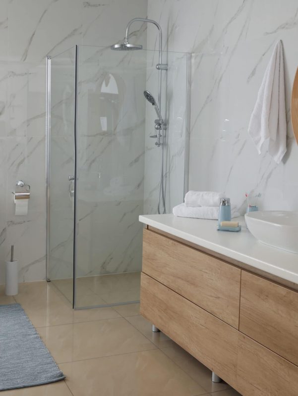 Modern bathroom with marble walls, glass shower enclosure, and wooden vanity with vessel sink. Brigh.